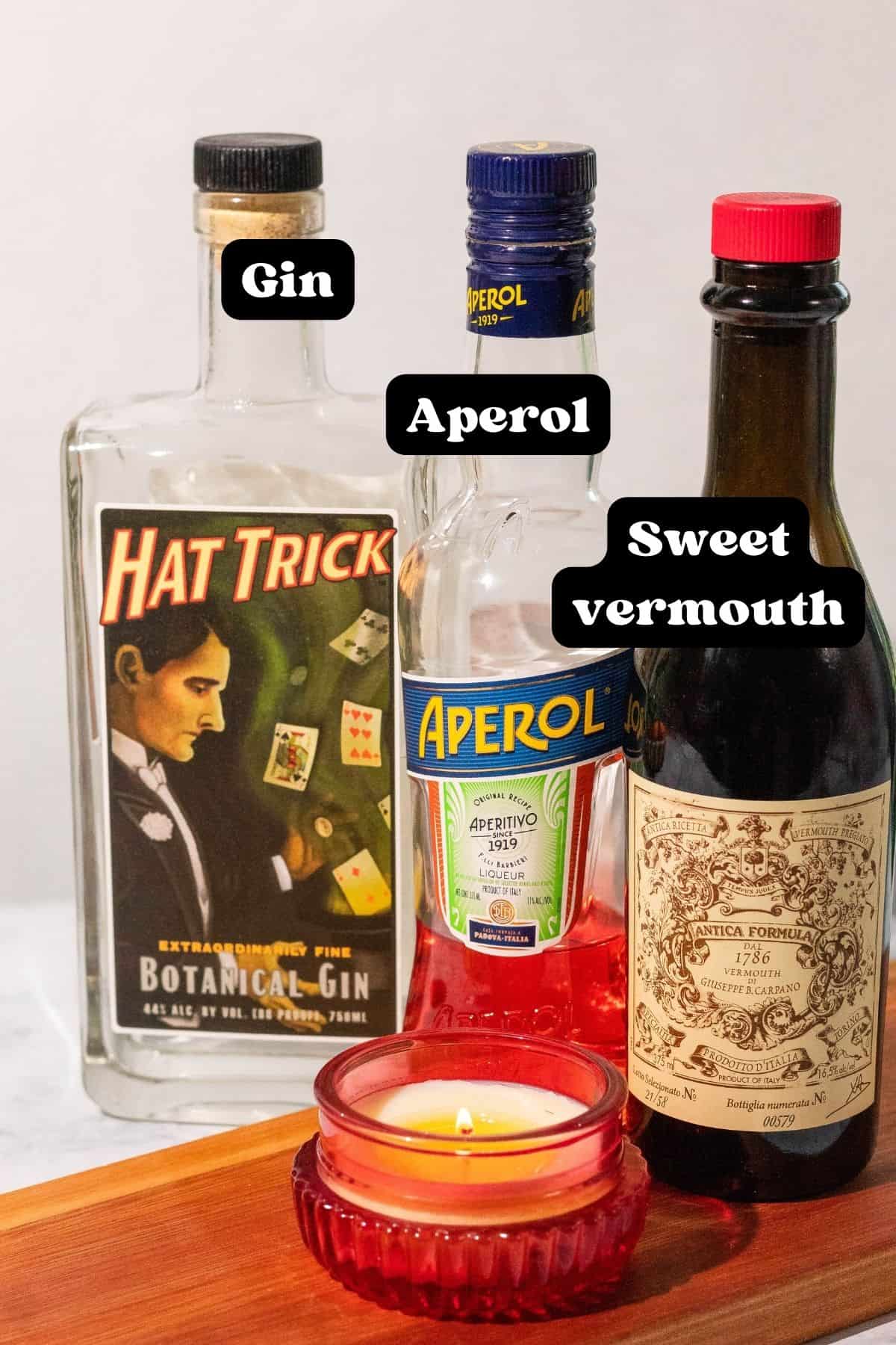 Ingredients shown with the text overlay "gin, aperol, and sweet vermouth" above each bottle with a red candle in the front.