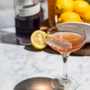 Passion fruit gin sidecar on a white marble table top with lemons and empress gin in the background.