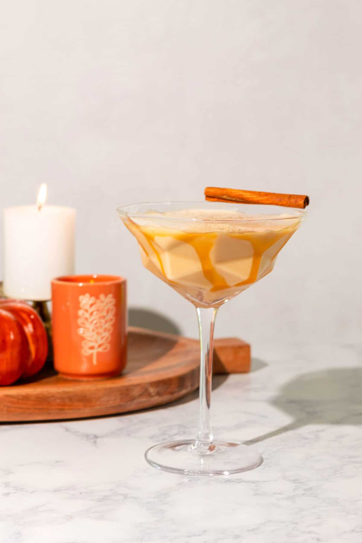 Pumpkin spice mudslide cocktail in a martini glass garnished with a cinnamon stick with candles and pumpkins in the background.