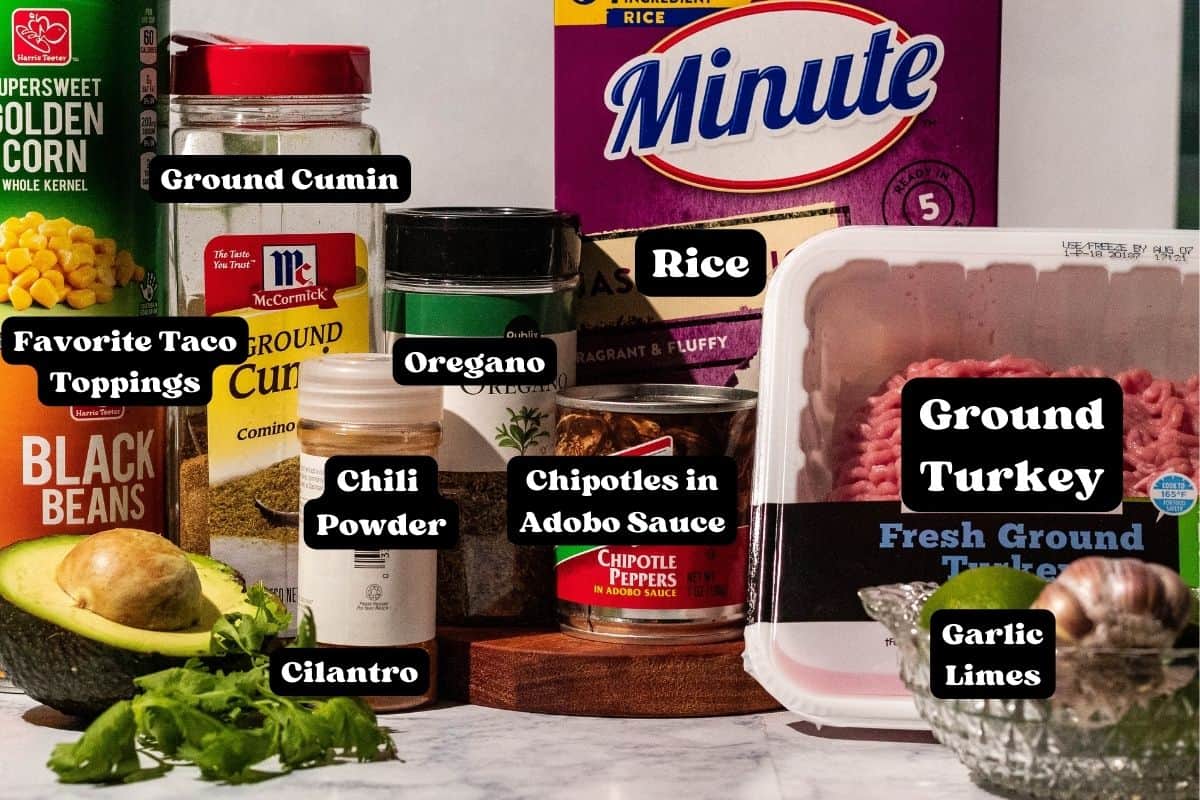 Ingredients for the taco bowls with ingredient names listed in black and white with the words "ground cumin, favorite taco toppings, cilantro, oregano, chili powder, chipotles in a adobo sauce, ground turkey, limes, garlic, and rice"