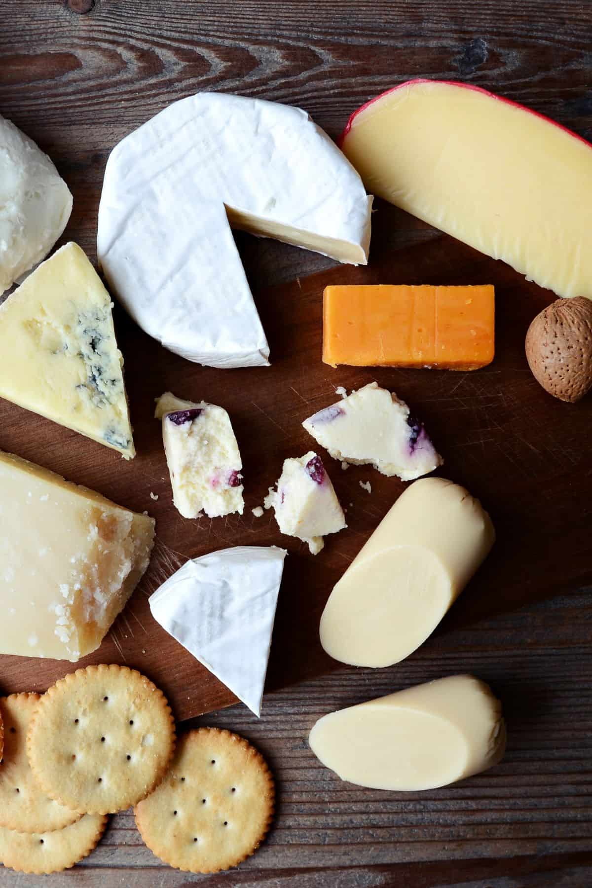 Several pieces of different cheeses on a brown cutting board. 