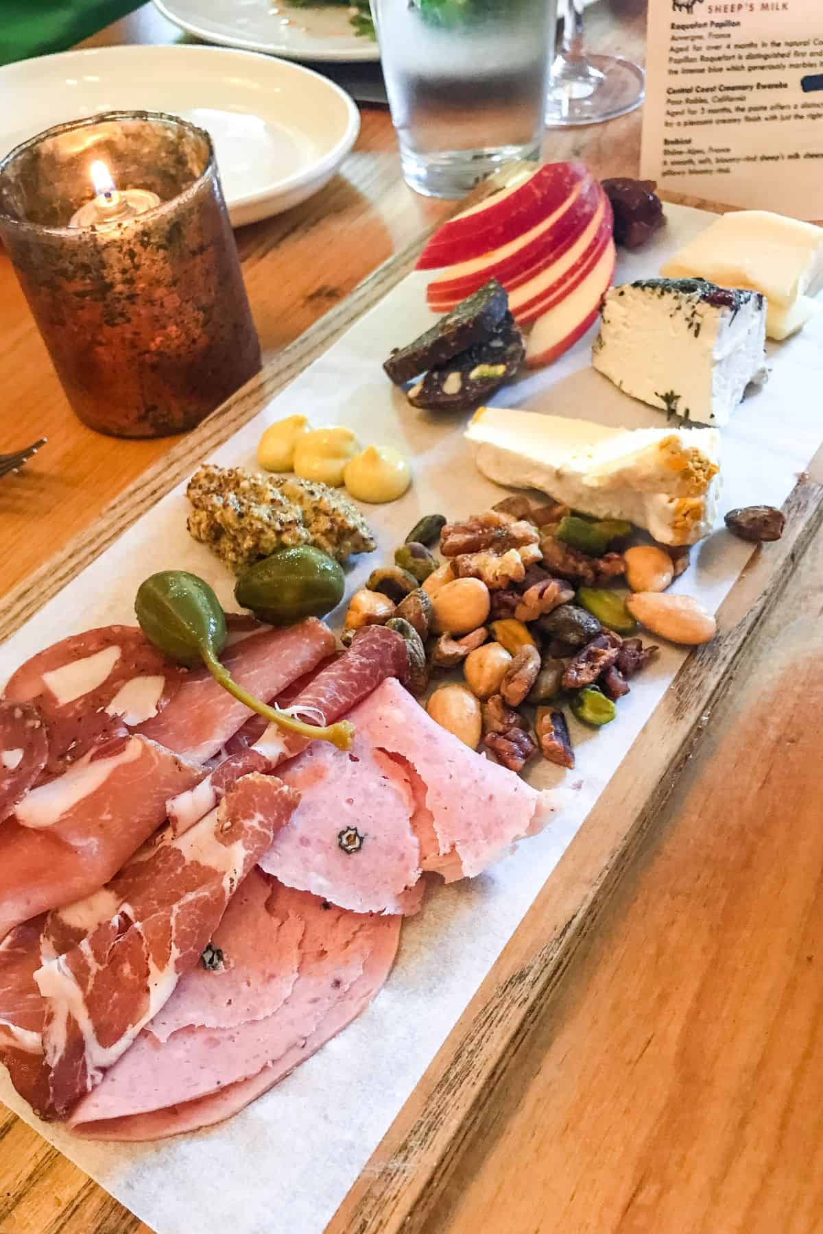 Long charcuterie board with meats, nuts, cheese, and fruit.