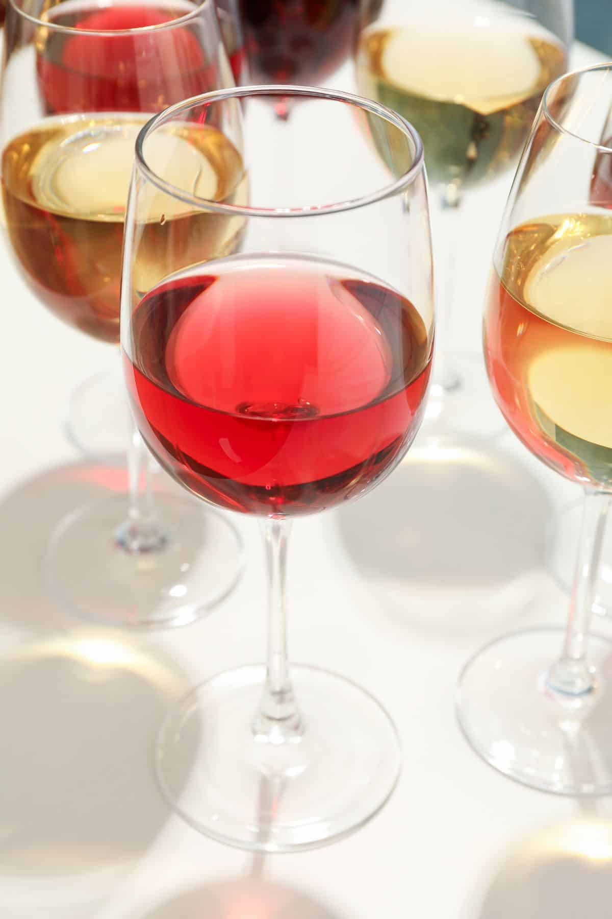 Several glasses of wine and red white on a white tabletop.
