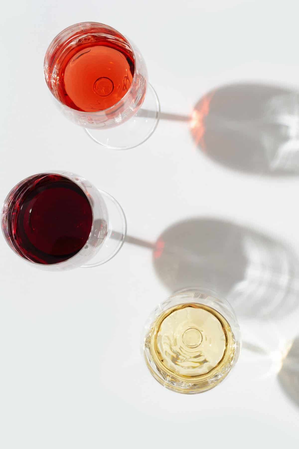 3 glasses of red, rose, and white wine on a white background.