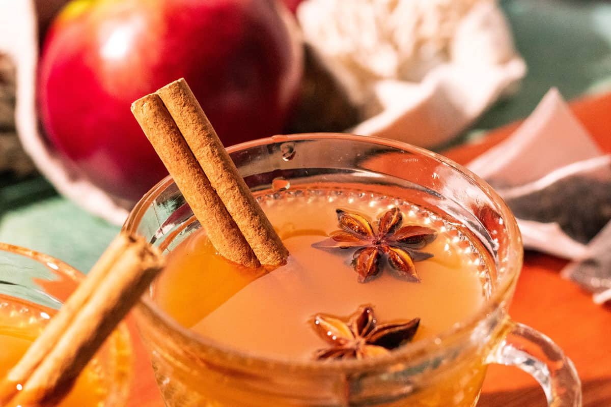 Glass mug of hot toddy with a cinnamon stick and two star anise pods floating on top.