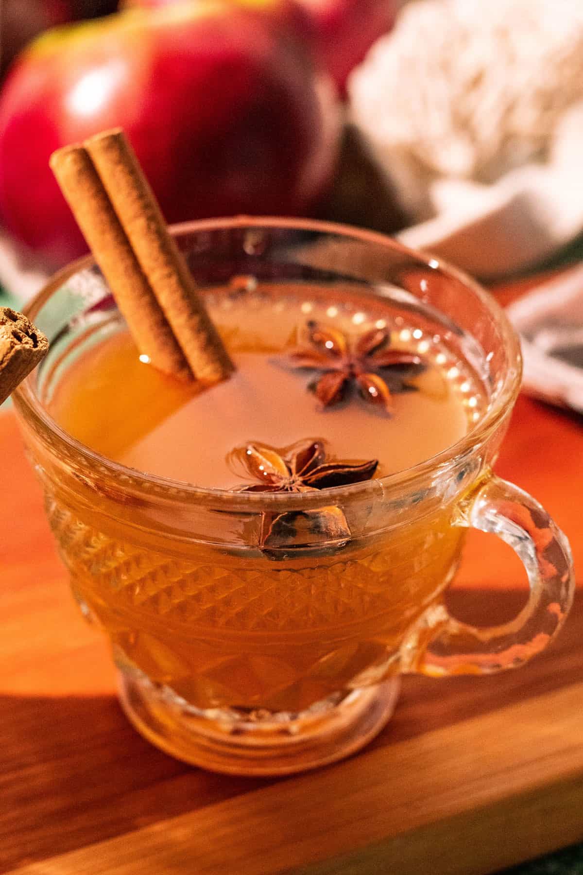 Glass mug of hot toddy with apples in the background.