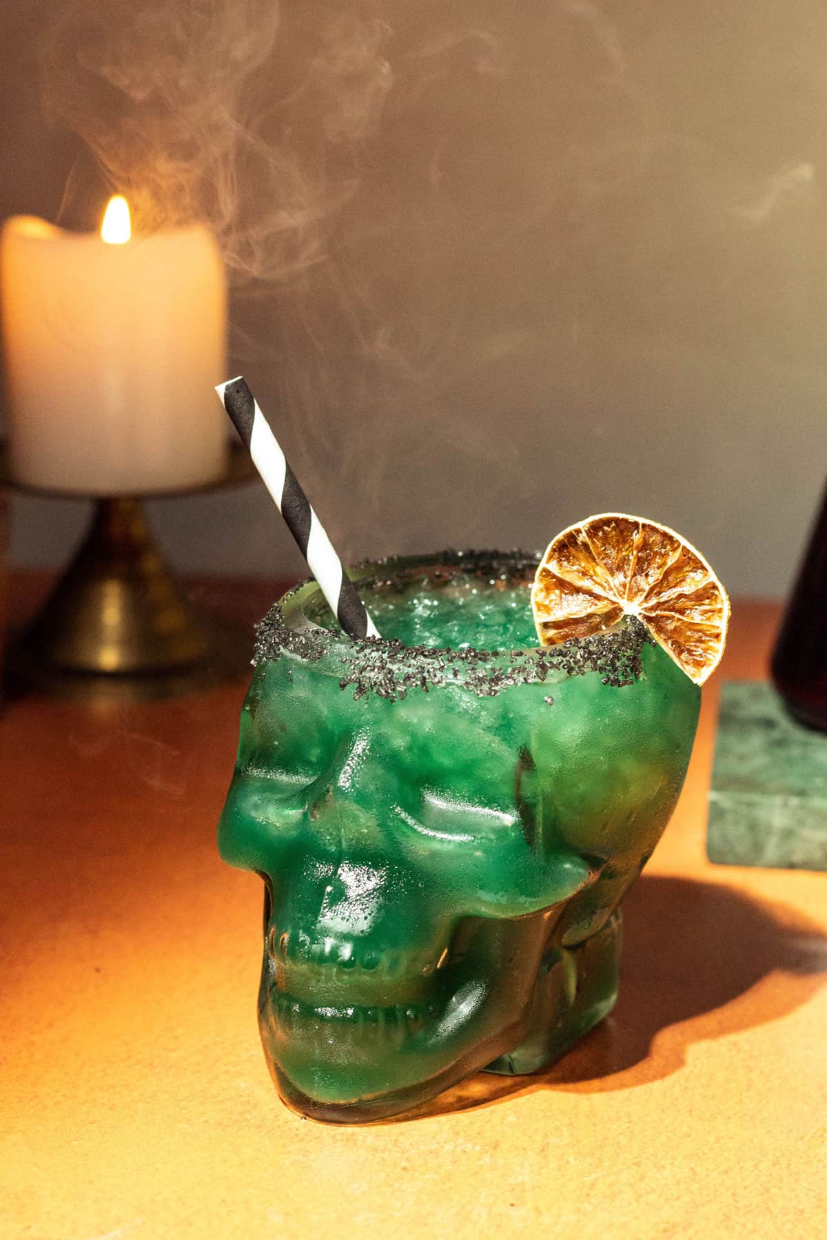 Green margarita in a skull glass with a dried lime and black/white straw for garnish.