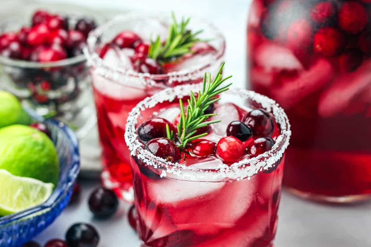 Two mistletoe margaritas garnished with rosemary and fresh cranberries.
