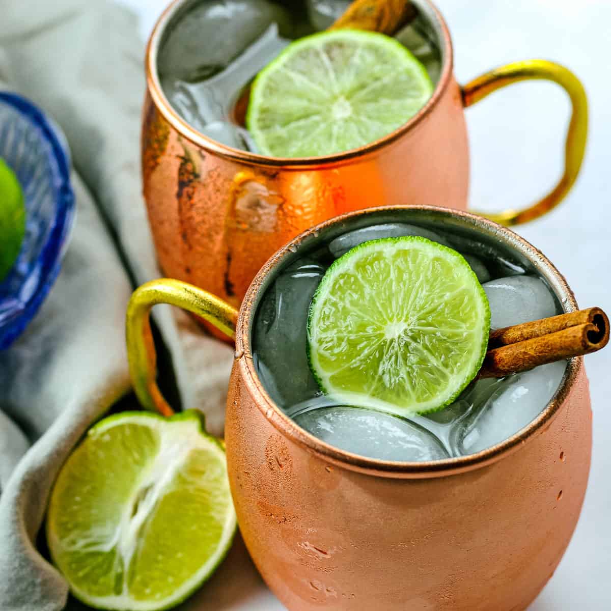Two bourbon mules in copper mugs with a bowl of limes.