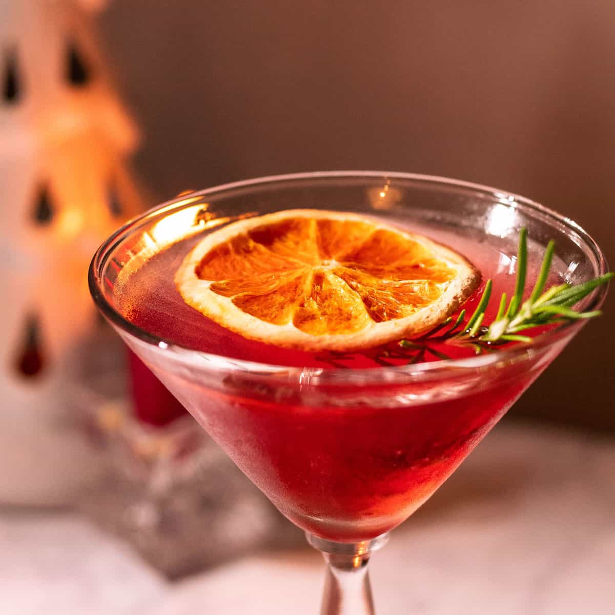 Martini glass with rosemary and dried orange wheel for garnish.