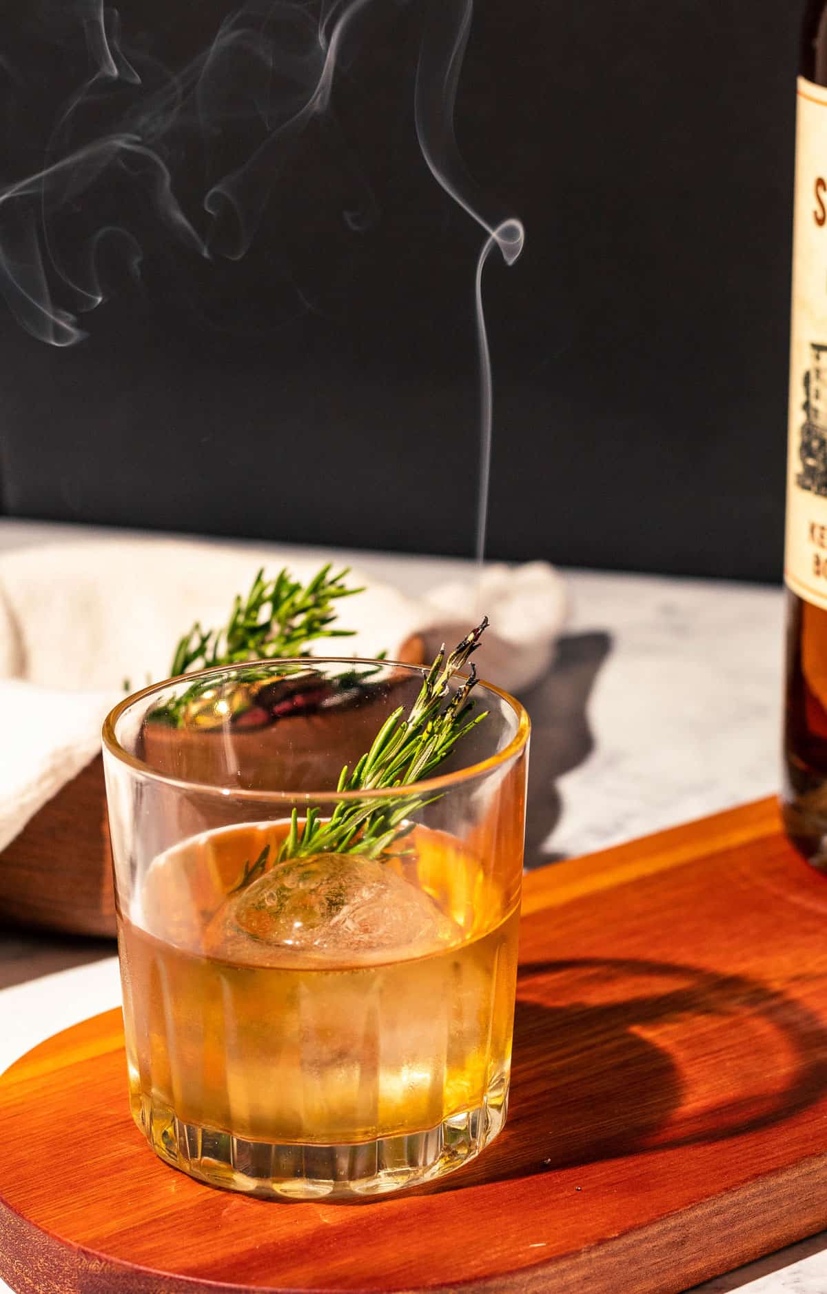 Old fashioned with smoke traveling upwards from the smoking rosemary sprig.