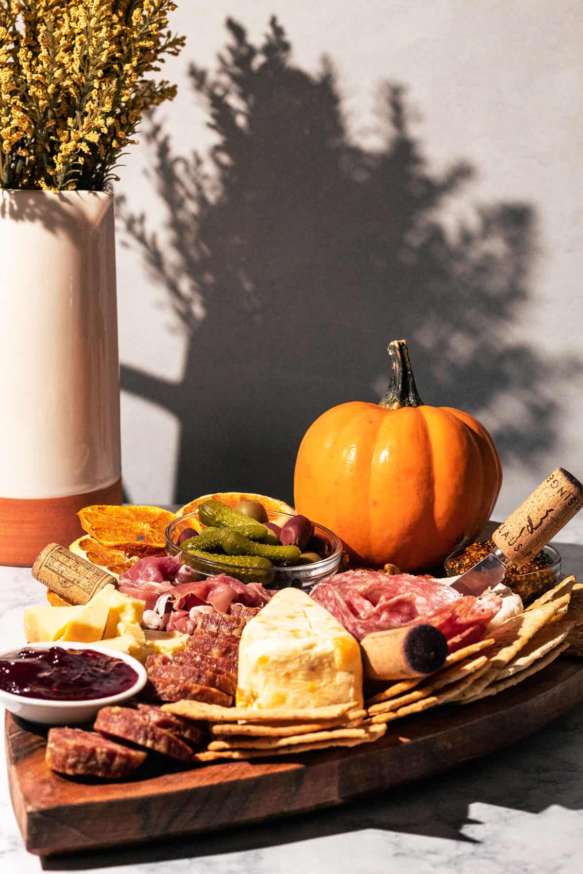 Thanksgiving charcuterie board with a vase of yellow flowers in the background.