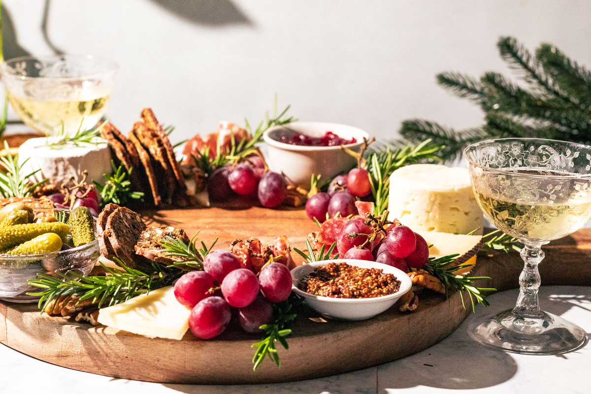 Wreath charcuterie board with glasses of champagne and greenery.
