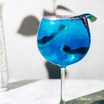 Blue shark cocktail in a large bowl shaped wine glass on a green and white marble surface.