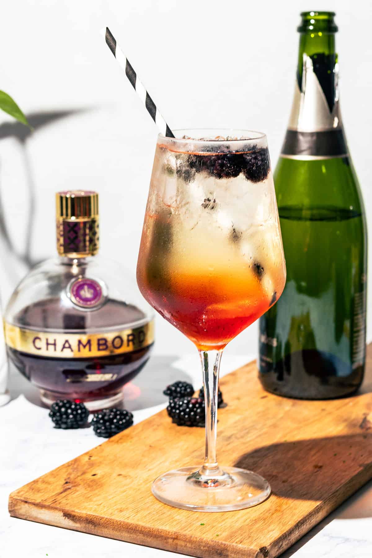 Spritz on a wood cutting board with a bottle of Champagne and Chambord in the background.