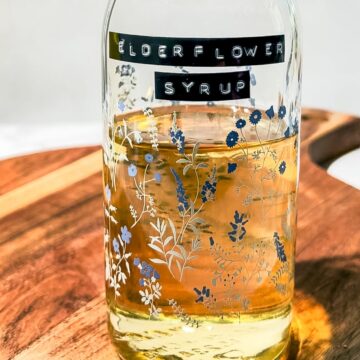 Bottle of syrup on a wood cutting board that is labeled "elderflower syrup" across the front.
