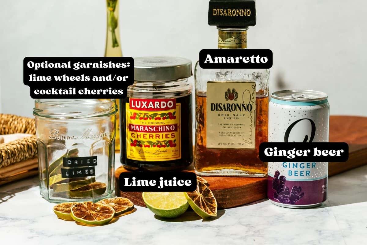 Ingredients for an Italian Mule cocktail spread out on a wood cutting board on a white marble counter.