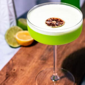 Midori sour cocktail on a wood cutting board.