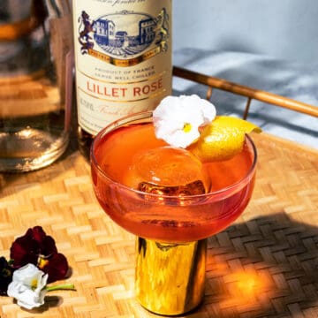 Negroni in a coupe glass with flowers on the side on top of a wicker tray.