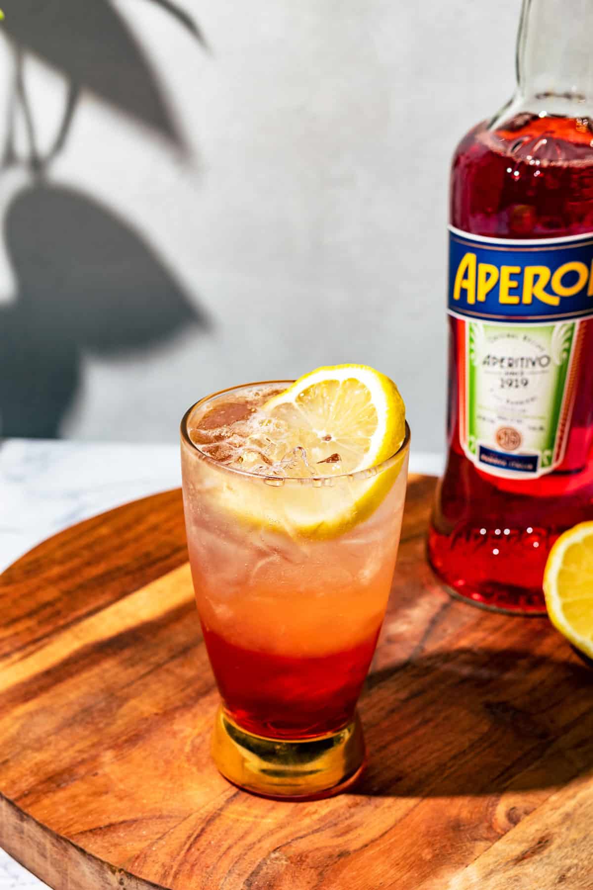 Aperol soda on a round wood cutting board with a bottle of Aperol in the background.