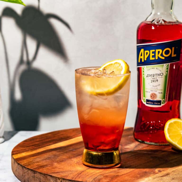 Aperol soda garnished with a lemon slice and a bottle of aperol and lemon half in the background.