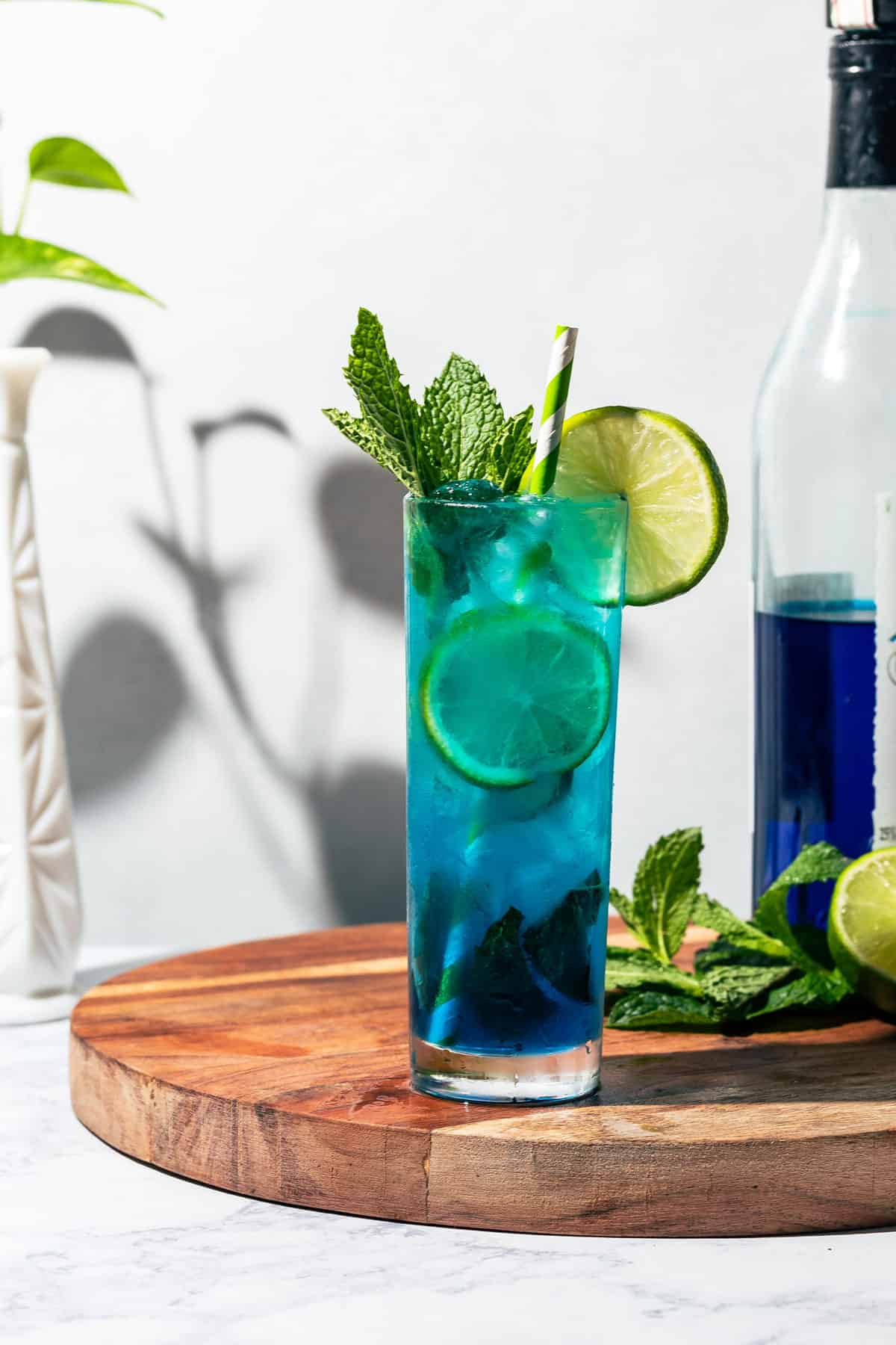 Blue mojito on a wood cutting board with mint and blue curacao in the background.