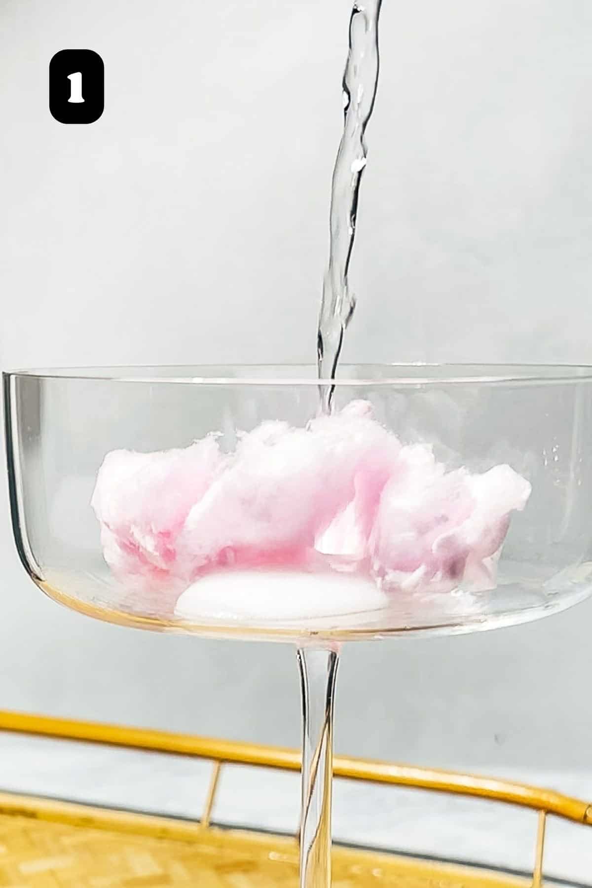 Step 1 showing prosecco being poured on top of the cotton candy in a coupe glass.
