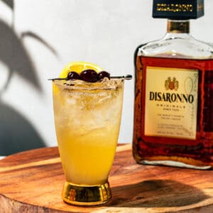 Fizz cocktail on wooden cutting board with a bottle of Disaronno in the background.