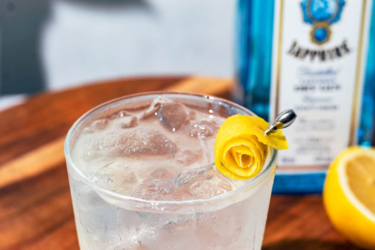 A rolled lemon peel rose sitting on top of the cocktail as a garnish.