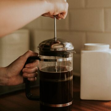 Hand pressing down on a plunger on a French Press.