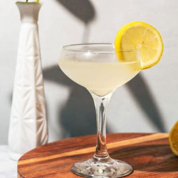 Lemon daiquiri on a wood cutting board with a white vase in the background.
