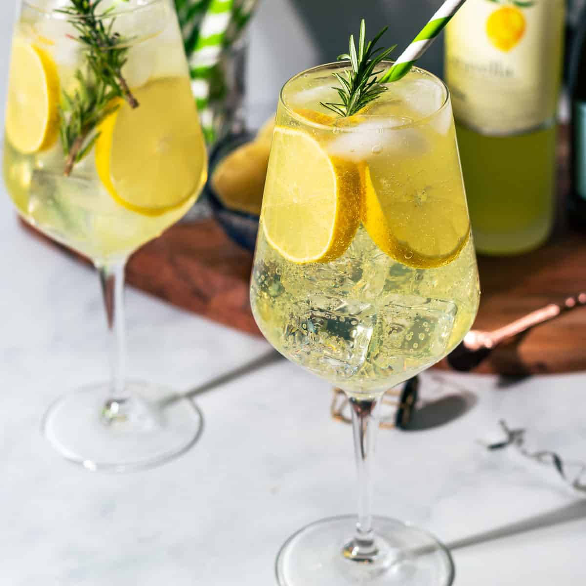 Limoncello spritz cocktails in wine glasses with a cutting board of ingredients in the background.