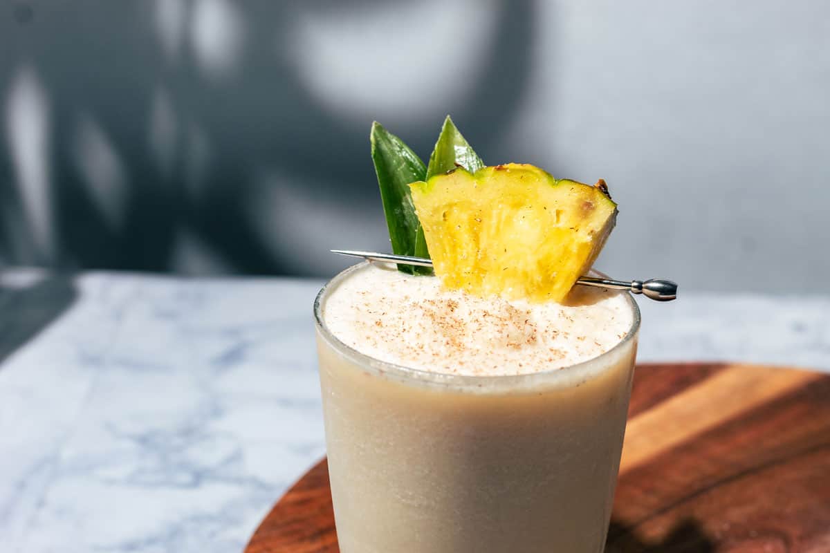 Pina colada mocktail garnished with a pineapple chunk and pineapple leaves.