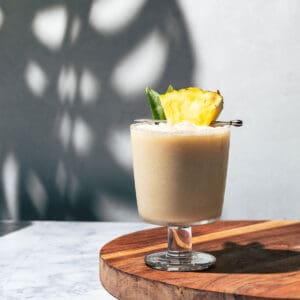 Pina colada mocktail in a glass goblet sitting on a round cutting board.