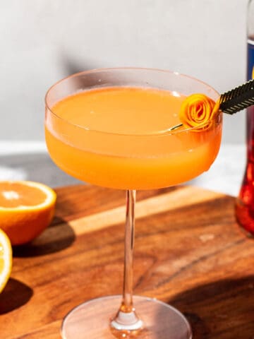 Martini with a rolled orange garnish on a wood surface.