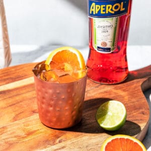 Mule cocktail on a wood surface with a bottle of Aperol in the background.