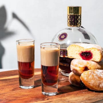 Shots on a wood surface with a stack of jam donuts and a bottle of Chambord in the background.