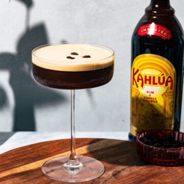 Espresso martini on a wood surface with a bottle of Kahlua in the background.