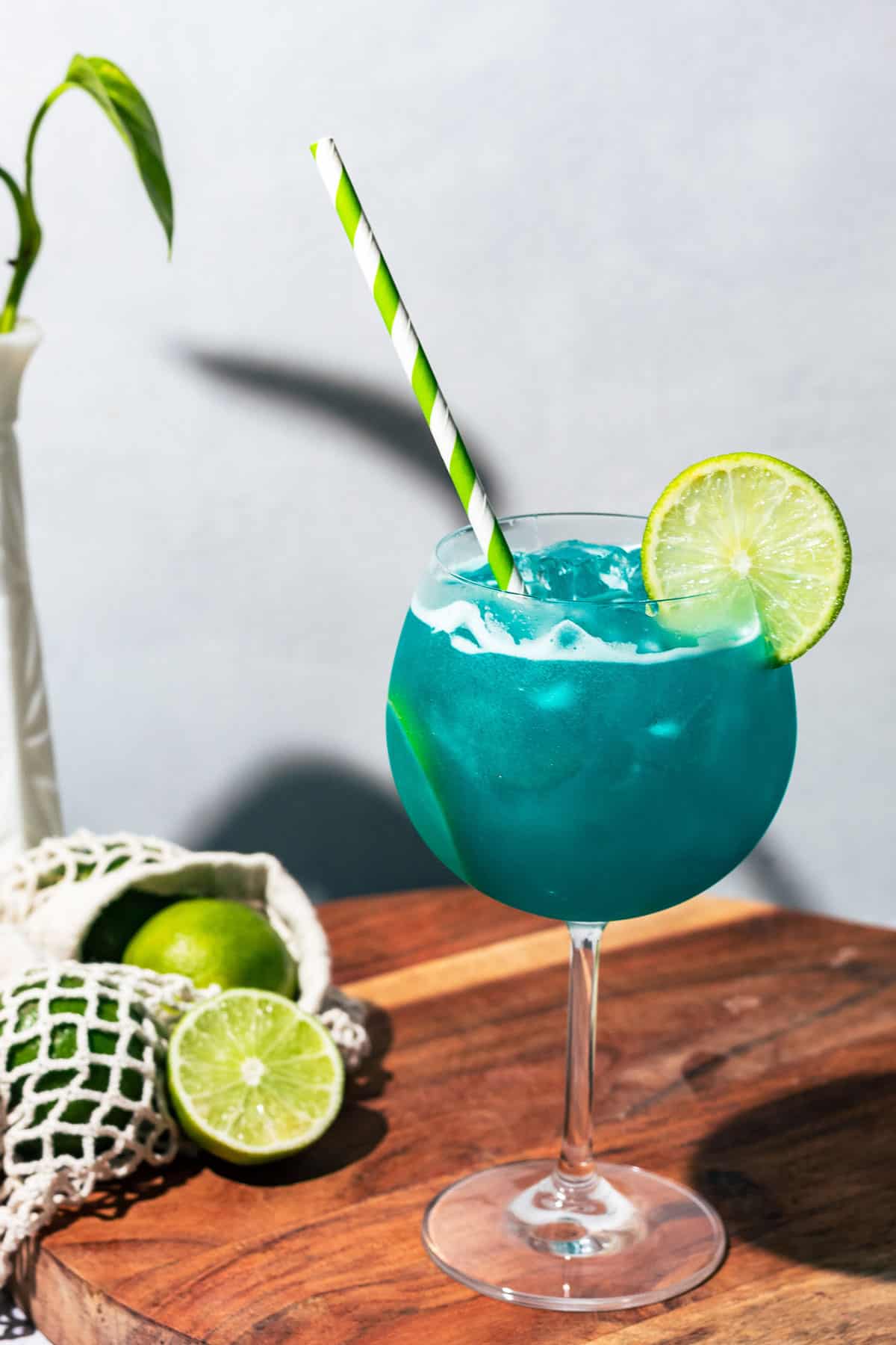 Mermaid Water Margarita on a wood surface with a green paper straw and lime slice garnish.