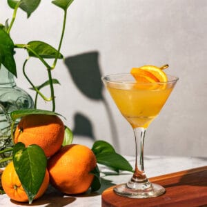 Orange creamsicle martini on a wood cutting board with greenery and fresh oranges in the background.