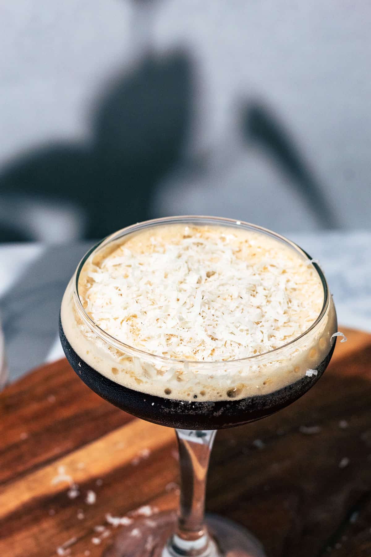 Espresso martini topped with shredded parmesan cheese on a wood surface.