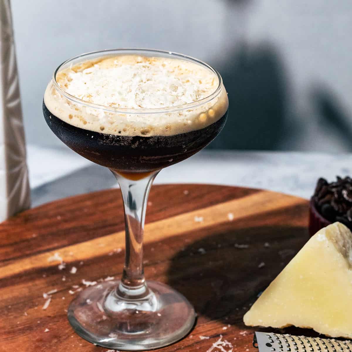 Espresso martini topped with shredded cheese and a block of parmesan with a grater on the side.
