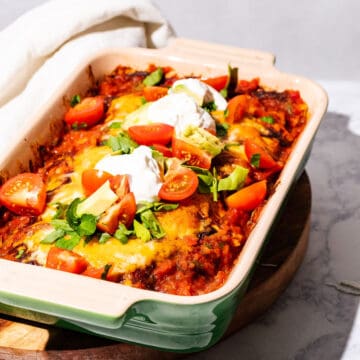 Enchilada casserole dish on a wood cutting board with a kitchen towel on the side.