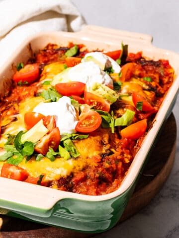Enchilada casserole dish on a wood cutting board with a kitchen towel on the side.