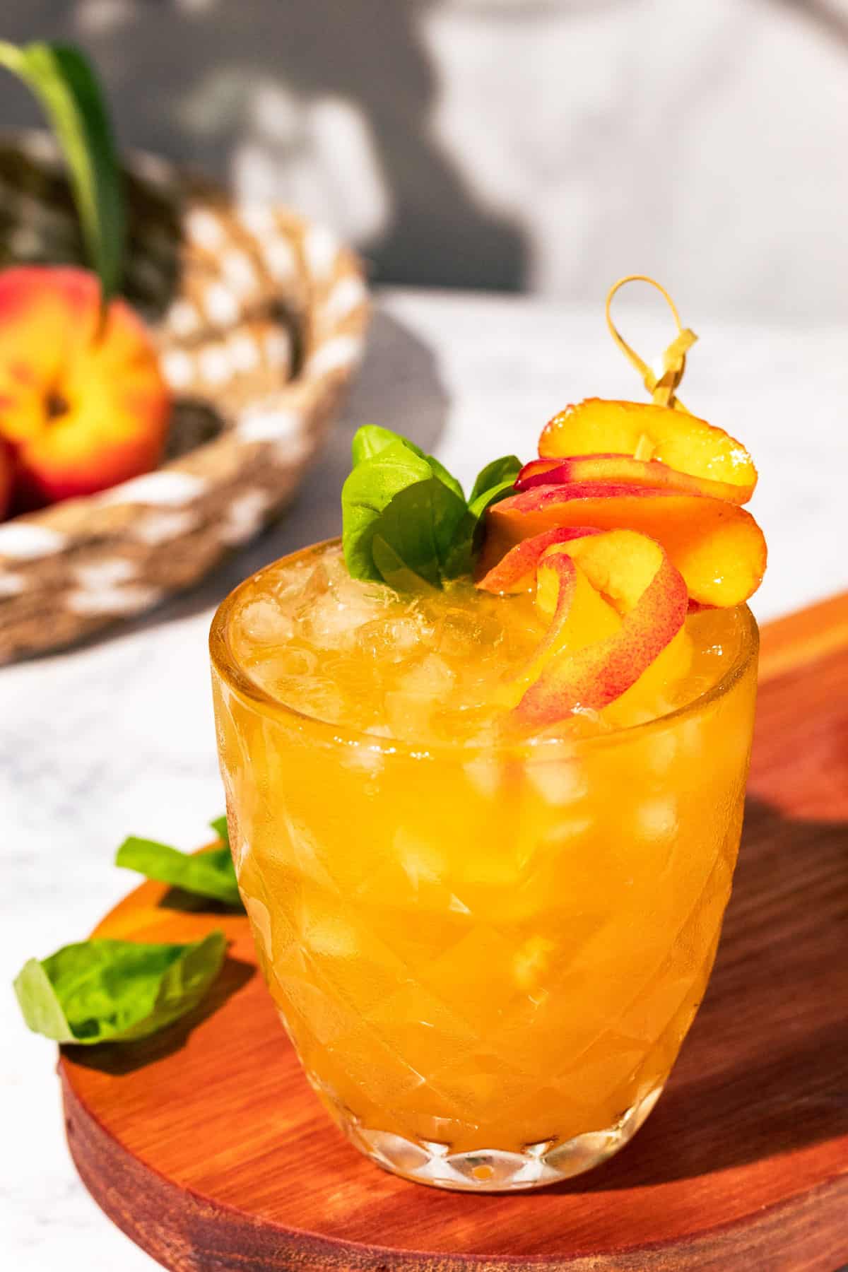 Bourbon peach smash on a wood surface garnished with peach slices and fresh basil.