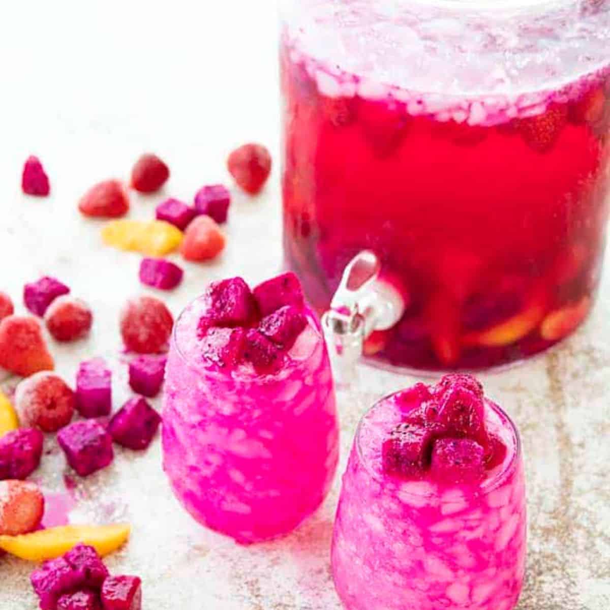 Bright pink cocktails with a drink dispenser in the background.