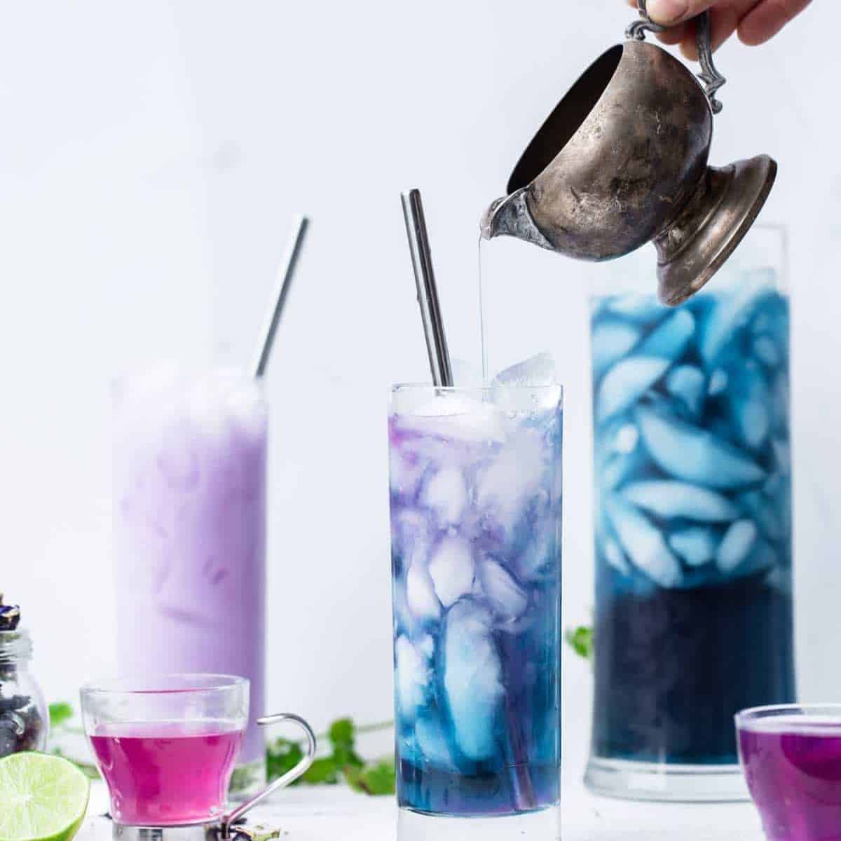Butterfly pea flower tea being poured into a tall glass with a straw.