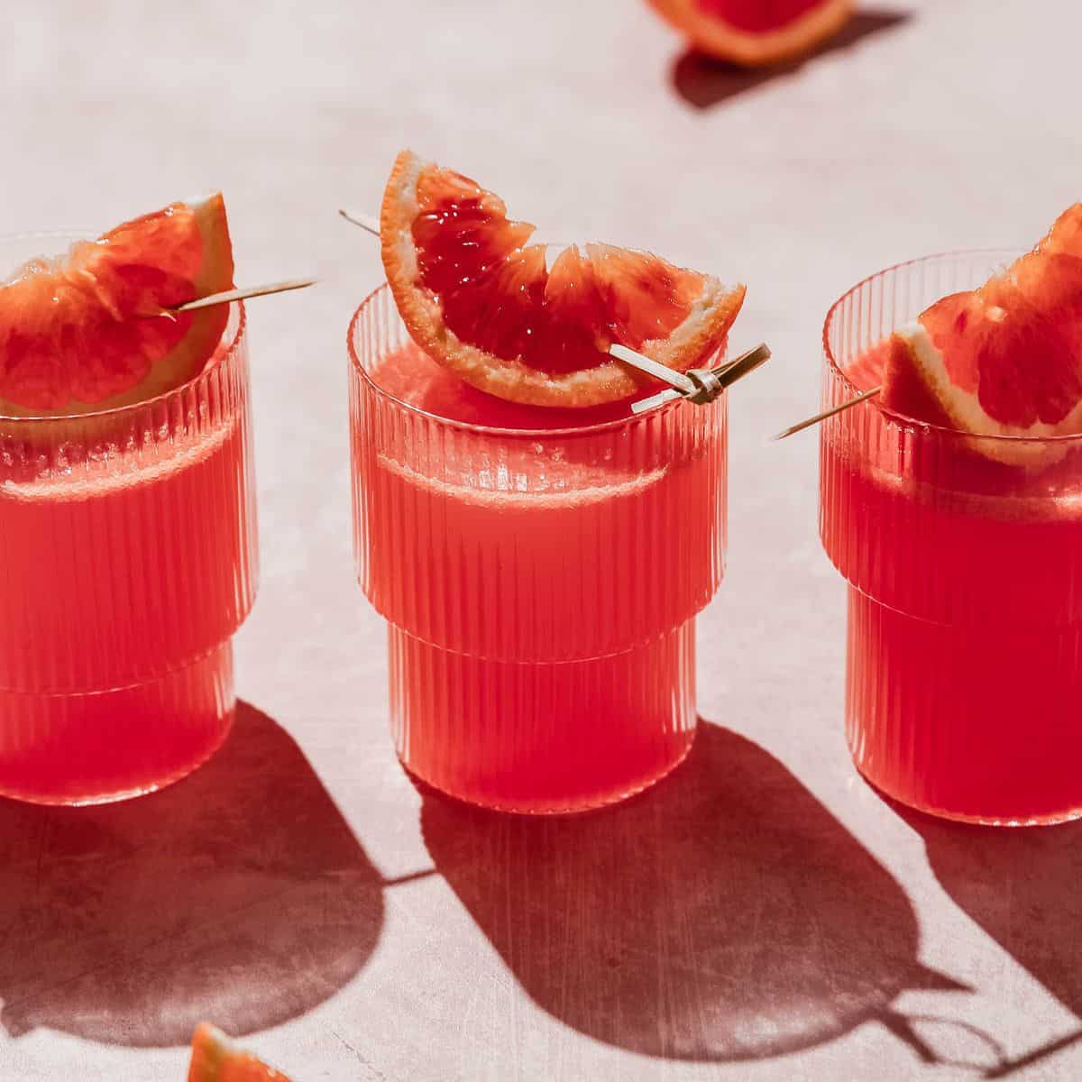 3 bright red cocktails on a white surface.