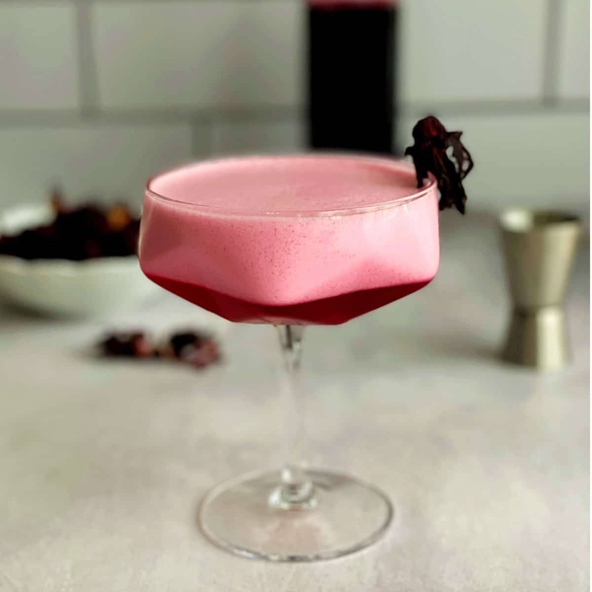 Bright red cocktail in a coupe glass with foam on top.