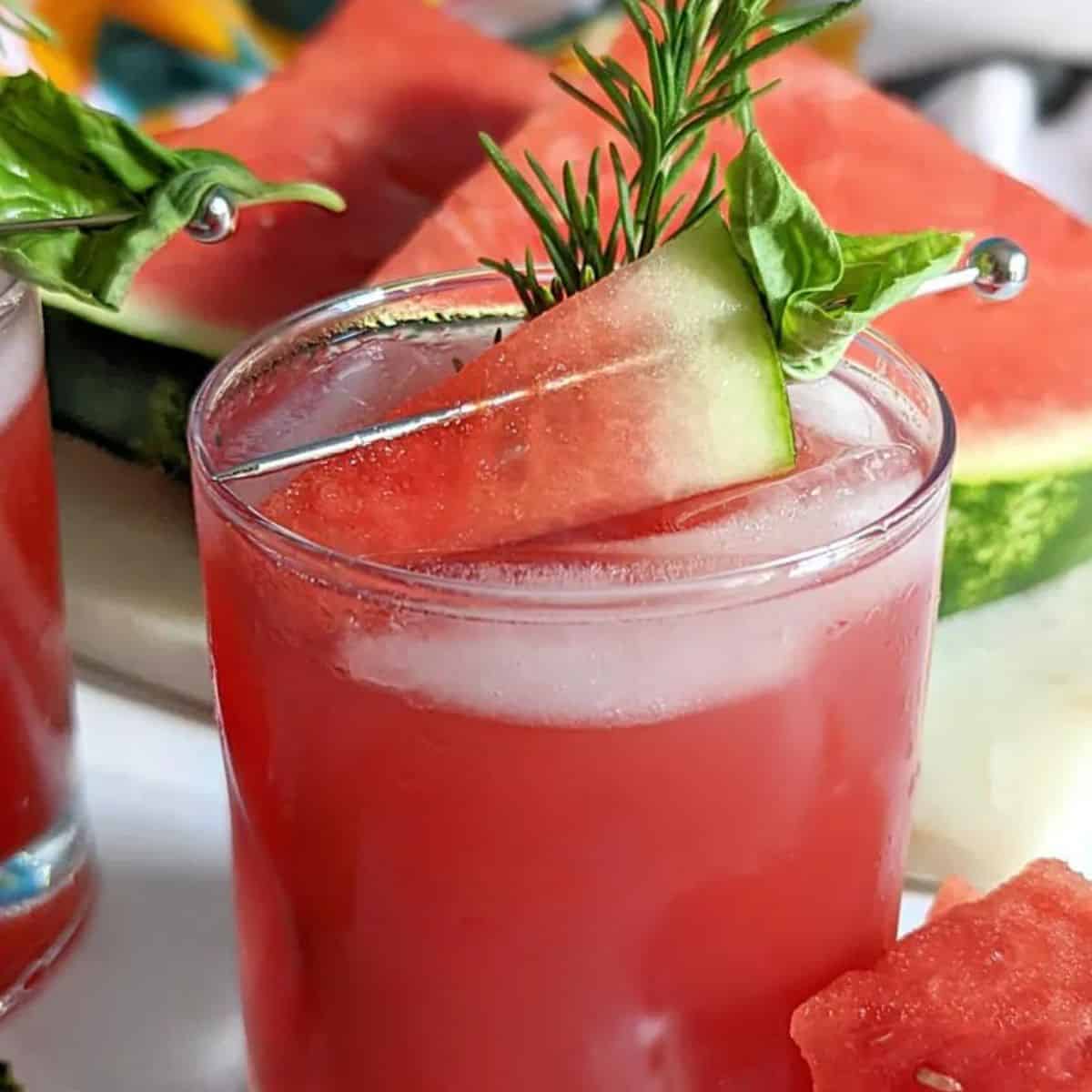 Watermelon cocktail garnished with herbs and watermelon slice.